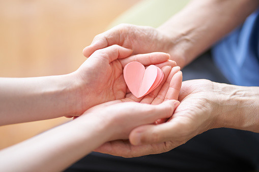 Hands of caregivers and elderly people with heart-shaped objects